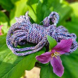 Bamboo bondage rope lilac coiled on green leaves with a purple flower accent